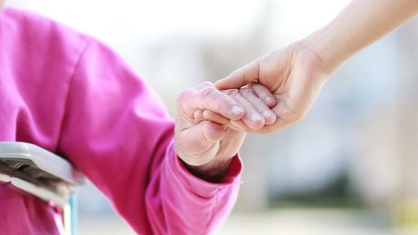 Photo of a young person's hand holding an elderly person's hand.