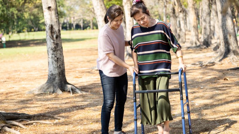 A woman supporting a woman with a walking frame