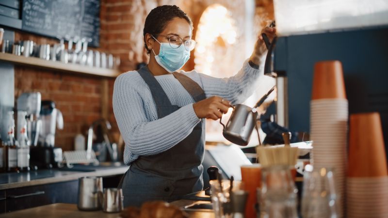 A barista wearing a mask is using a coffee machine.