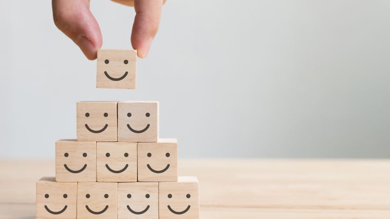 There is a pyramid of cubes with smiley faces on them. A hand is placing a cube on the top.