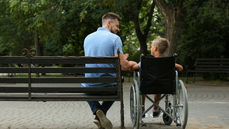 Adult on a bench sits next to child in a wheelchair