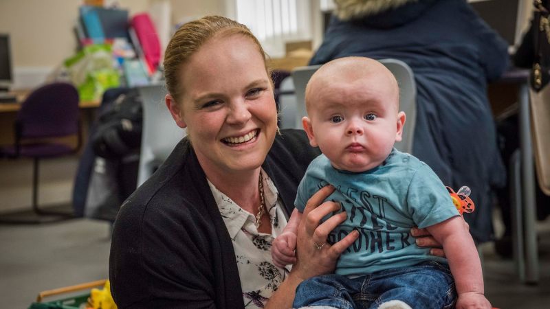 Mother holding a baby on her knee and smiling at the camera