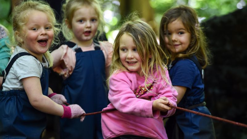 Group of children play tug a war in a forest.