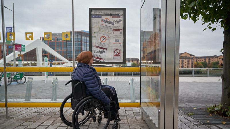 Female in wheelchair reading information at a bus stop